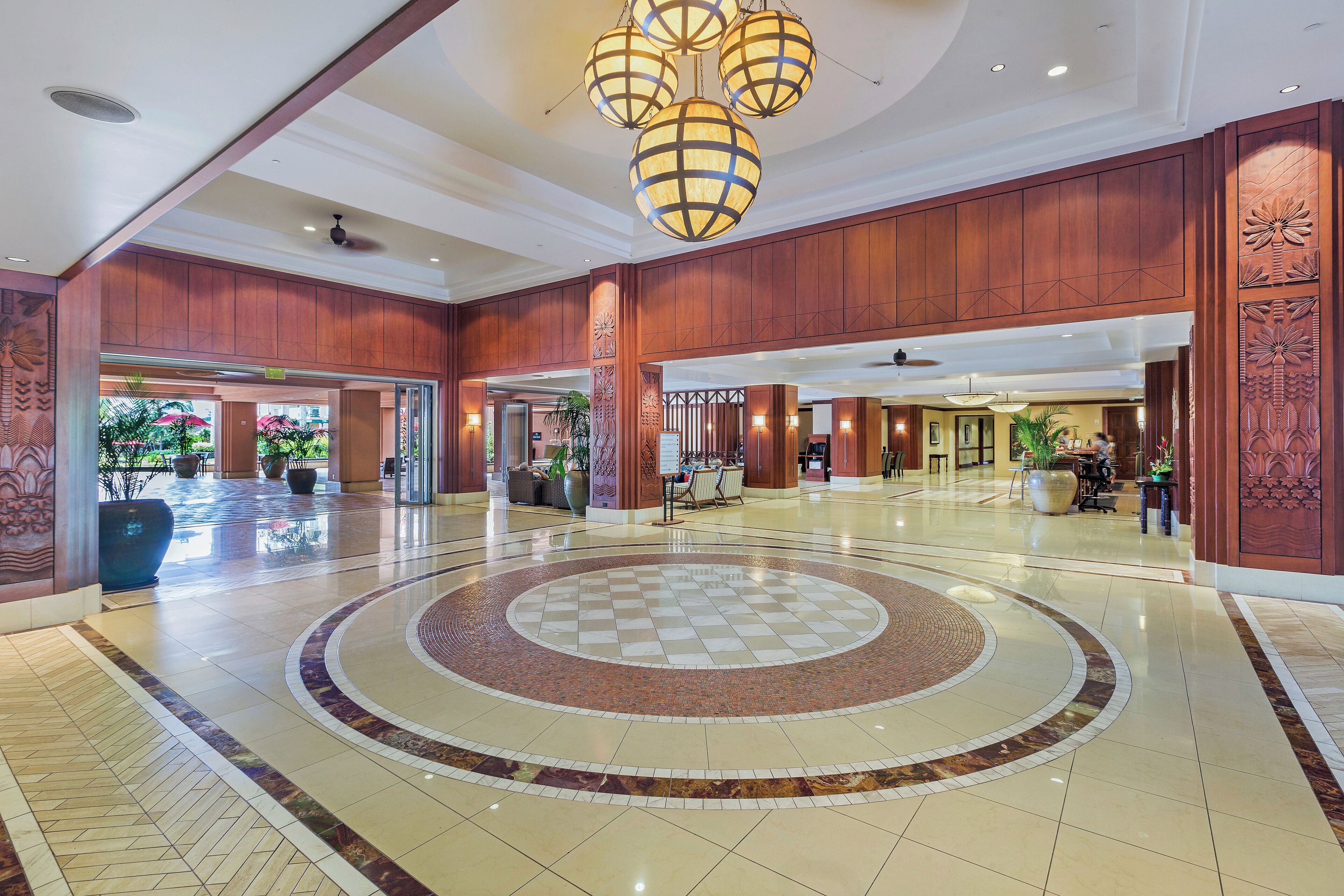 A spacious lobby with a circular patterned floor, wooden paneling, and a central chandelier.
