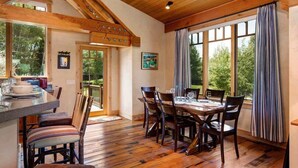 A dining area with a wooden table and chairs, a kitchen area with a counter and stools, and large windows with curtains. - Abode at Skyline, outdoor living, mountain views (Jackson)