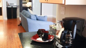 A kitchen area with a coffee maker, two mugs on a red plate, a blue couch, and a dining table.