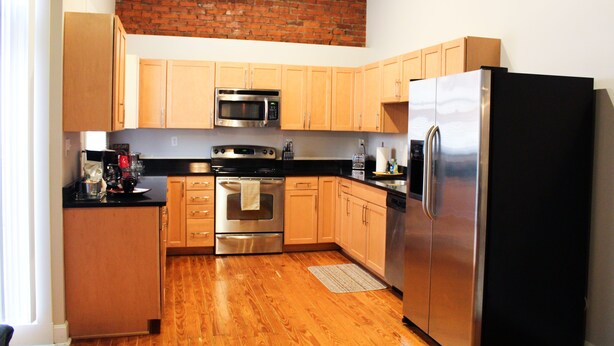 A kitchen with wooden cabinets, stainless steel appliances, and a brick wall.