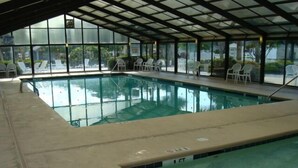 Une piscine intérieure avec des parois en verre transparent, des chaises longues et un sol carrelé.