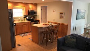 Une cuisine moderne avec des meubles en bois, un îlot central doté de tabourets, un four à micro-ondes et un réfrigérateur.