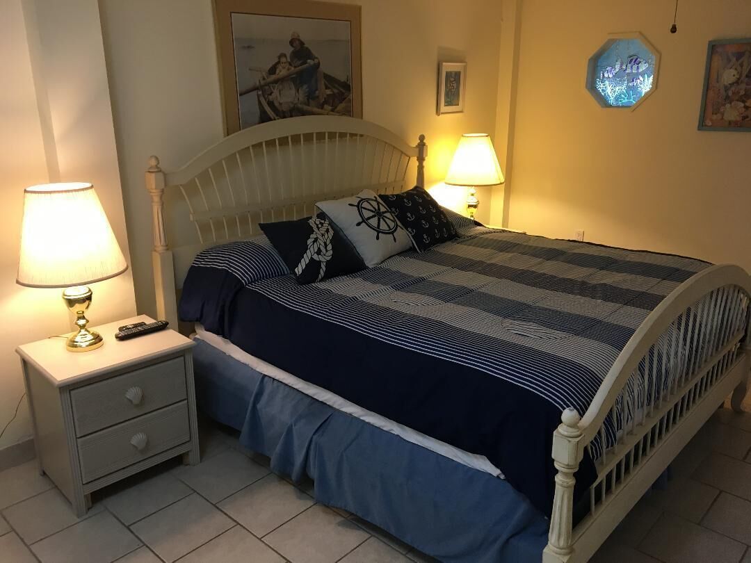 A neatly made bed with a striped bedspread and matching pillows, a bedside table with a lamp, and a wall-mounted picture.