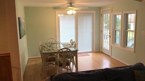 Un espace repas comprenant une table et des chaises, un ventilateur de plafond et une porte-fenêtre coulissante donnant sur l’extérieur.