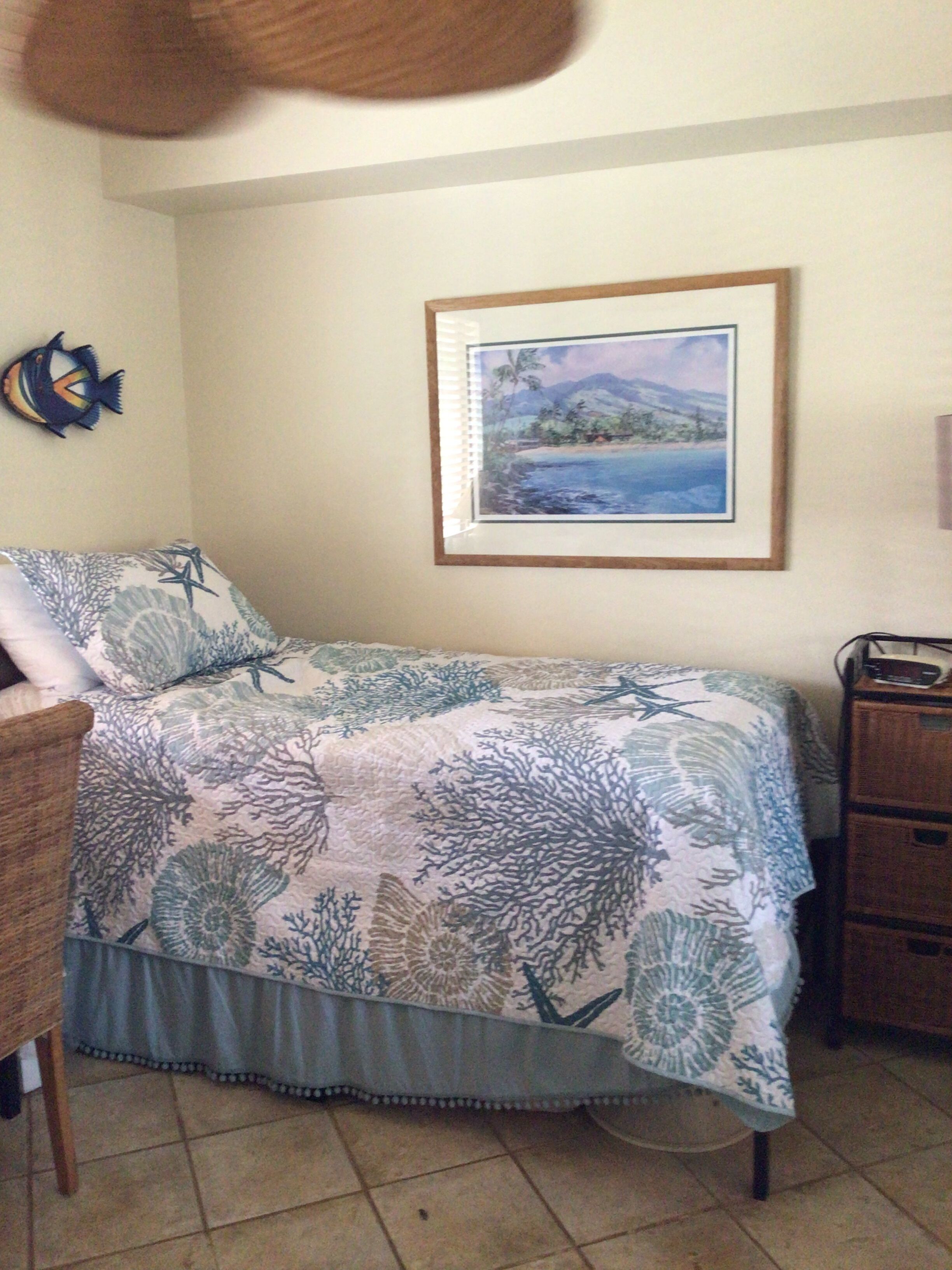 Une chambre à coucher avec un lit, un tableau encadré au mur, une petite décoration en forme de poisson et une commode en bois.