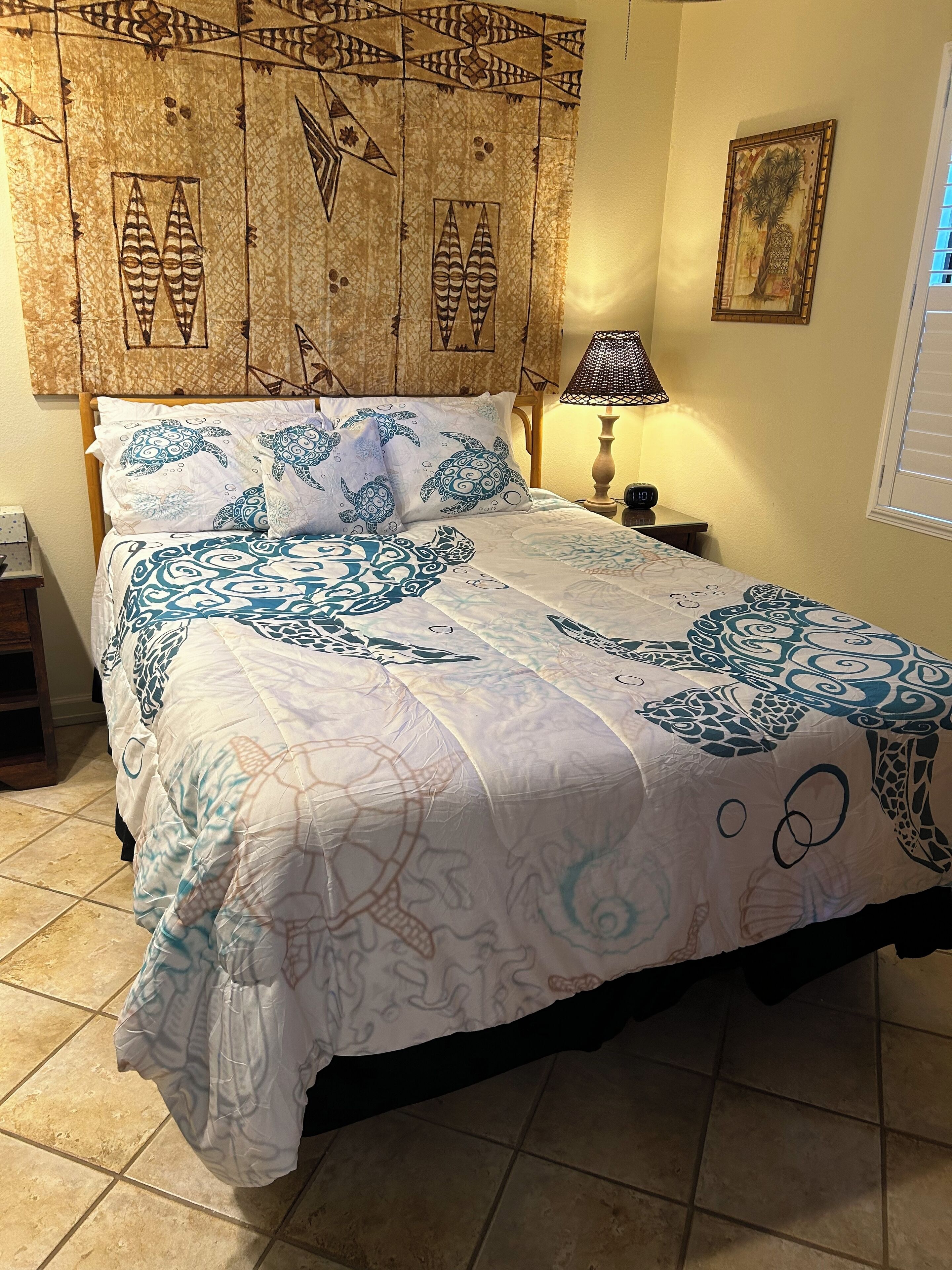 A bed with a patterned bedspread, a headboard with decorative panels, a bedside lamp, and a framed picture on the wall.