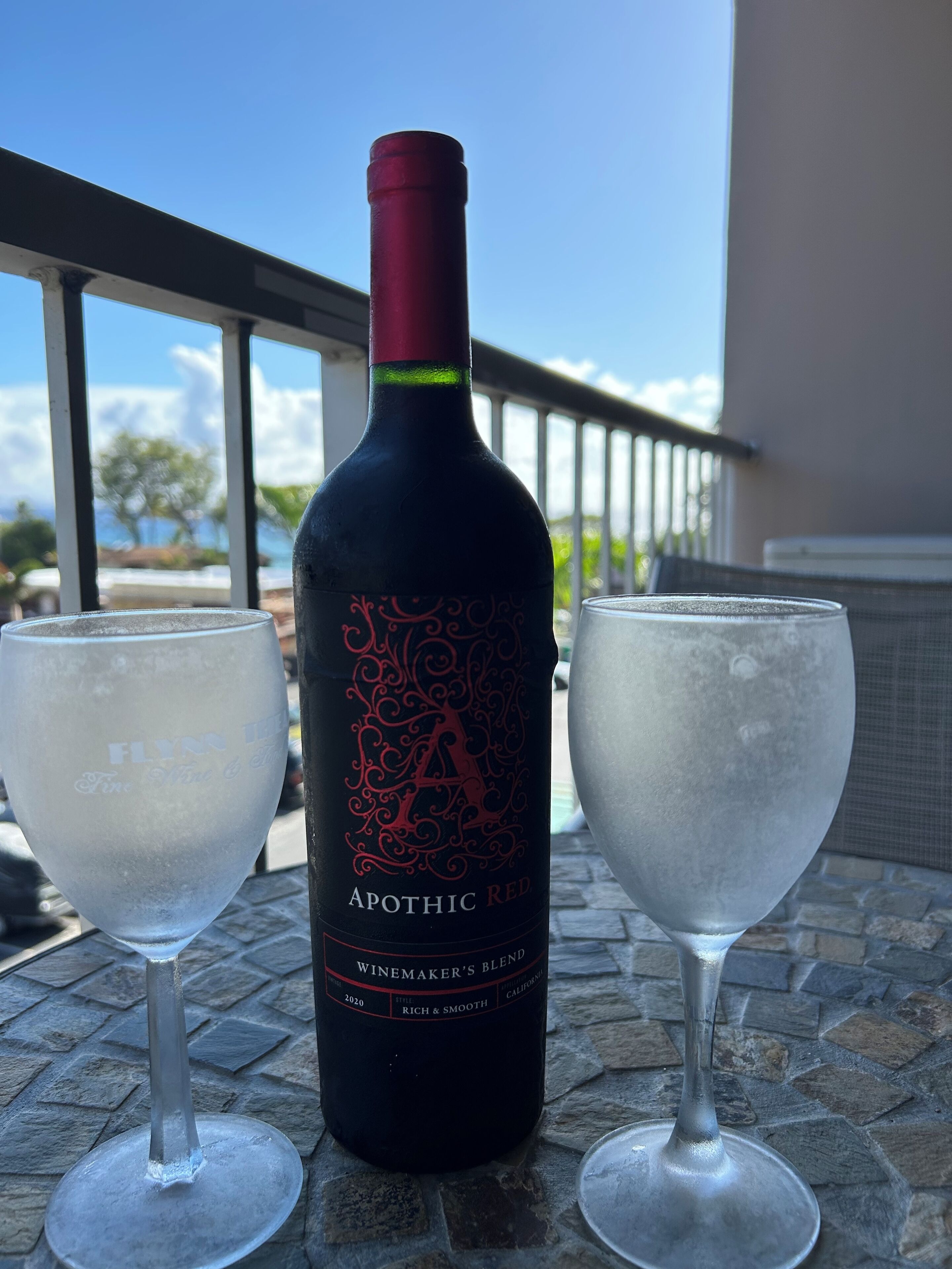 Una botella de vino tinto Apothic sobre una mesa con dos copas.