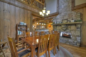A wooden dining area with a stone fireplace, wooden chairs, and a chandelier. - Reel Creek Lodge - Fightingtown Creek (Blue Ridge)