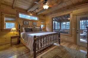 A wooden cabin bedroom with a bed, bedside lamps, and a view through large windows. - Reel Creek Lodge - Fightingtown Creek (Blue Ridge)