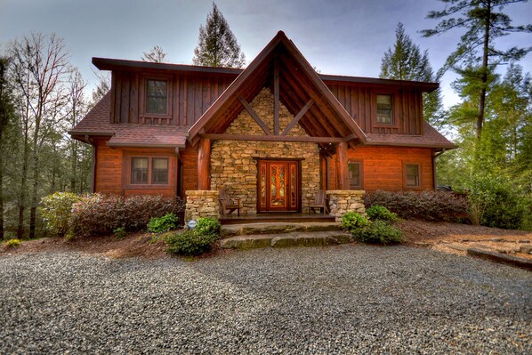 A two-story log cabin with a stone foundation, wooden exterior, and a prominent front porch with two chairs. - Reel Creek Lodge - Fightingtown Creek (Blue Ridge)