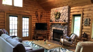 A cozy log cabin interior with a stone fireplace, wooden walls, a sofa, a chair, and a television. - Log Cabin on Garfield Lake near Walker MN (Laporte)