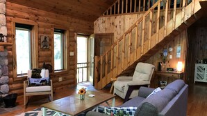A cozy cabin interior with a wooden staircase, a sofa, a chair, and a dining table. - Log Cabin on Garfield Lake near Walker MN (Laporte)