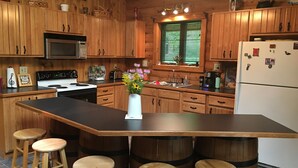 A kitchen with wooden cabinets, a central island with stools, a stove, a microwave, and a refrigerator. - Log Cabin on Garfield Lake near Walker MN (Laporte)
