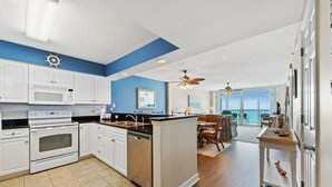 Una cocina moderna con armarios blancos, una isla central y un comedor con vista al océano.