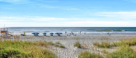 A beach with a lifeguard tower, beach umbrellas, and people enjoying the shore.