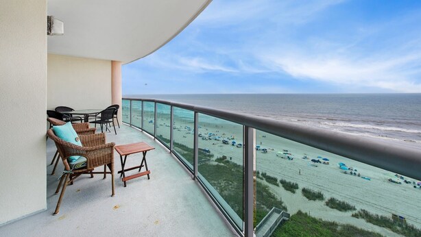 Un balcón con mobiliario de mimbre, una mesa y vistas a la playa y el océano.