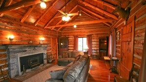 A log cabin interior with a stone fireplace, a sofa, a ceiling fan, and wooden walls. - Authentic Mountain Log Cabin Perched On A Cliff Side Above The Shenandoah River (Front Royal)