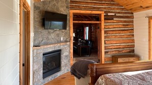 A log cabin interior with a stone fireplace, a mounted TV, and a ceiling fan. - Authentic Mountain Log Cabin Perched On A Cliff Side Above The Shenandoah River (Front Royal)