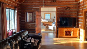 A cozy log cabin interior with a leather sofa, a TV, and a dining area. - Authentic Mountain Log Cabin Perched On A Cliff Side Above The Shenandoah River (Front Royal)