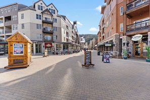 A paved pedestrian area with multi-story buildings, a wooden kiosk, and a signboard.