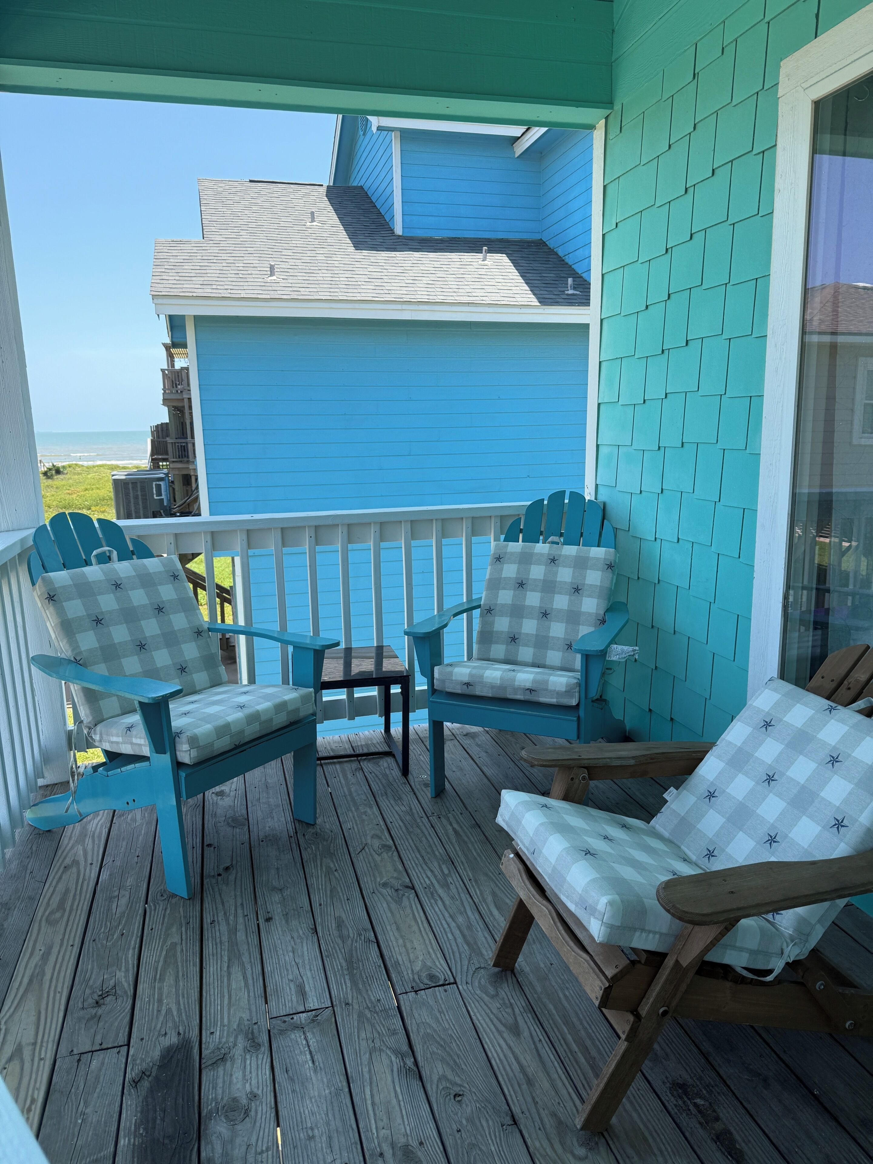 A wooden deck with two Adirondack chairs and a small table.