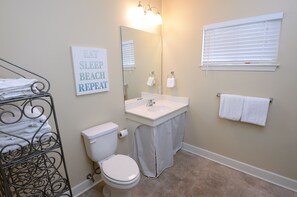 Ein Badezimmer mit Toilette, Waschbecken und Handtuchhalter. Ein Schild zeigt die Aufschrift 'EAT SLEEP BEACH REPEAT'.