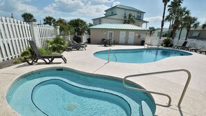 A pool area with lounge chairs and a small table, surrounded by a white fence and palm trees. - The Palms Studio, whirlpool, pool (Panama City Beach)
