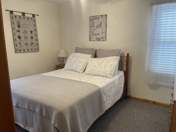 A bedroom with a bed, pillows, a nightstand, a lamp, and two wall decorations. - RELAX & GETAWAY IN A FULY FURNISHED CABIN IN THE BLUE RIDGE SMOKEY MOUNTAINS. (Maggie Valley)
