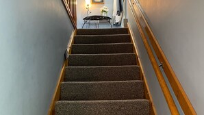 A carpeted staircase with wooden handrails, a wall-mounted clock, and a small table with a vase of flowers. - RELAX & GETAWAY IN A FULY FURNISHED CABIN IN THE BLUE RIDGE SMOKEY MOUNTAINS.  (Maggie Valley)