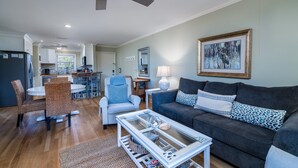 A spacious living room with a grey sofa, a glass coffee table, and a dining area with wicker chairs. - 2BR w/ Marsh Views! Walk to Tennis/Lake House! Amenities included!Pet Friendly! (Seabrook Island)
