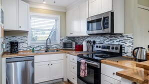 A modern kitchen with white cabinets, stainless steel appliances, a tiled backsplash, and a window with blinds. - 2BR w/ Marsh Views! Walk to Tennis/Lake House! Amenities included!Pet Friendly! (Seabrook Island)