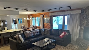A modern living room with a sectional sofa, a coffee table, and a fireplace. There is a dining area with a table and chairs, and a kitchen in the background. - Lovely Phoenix 2bd. walk to base or take shuttle, pool/hot tub, garage,  ++ (Steamboat Springs)