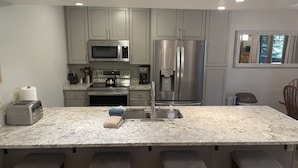 A modern kitchen with grey cabinets, stainless steel appliances, a marble countertop, and bar stools. - Lovely Phoenix 2bd. walk to base or take shuttle, pool/hot tub, garage,  ++ (Steamboat Springs)