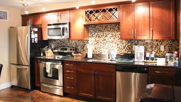 A modern kitchen with stainless steel appliances, wooden cabinets, and a tiled backsplash. - Welcome to Derby City Loft! (Louisville)