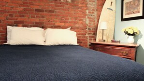 A bed with white pillows, a dark blue quilt, a wooden nightstand with a lamp, and a vase with flowers. - Welcome to Derby City Loft! (Louisville)