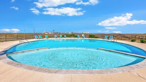 Una piscina grande y curvada con agua azul cristalina, rodeada por un muro de piedra bajo y una cerca de metal.