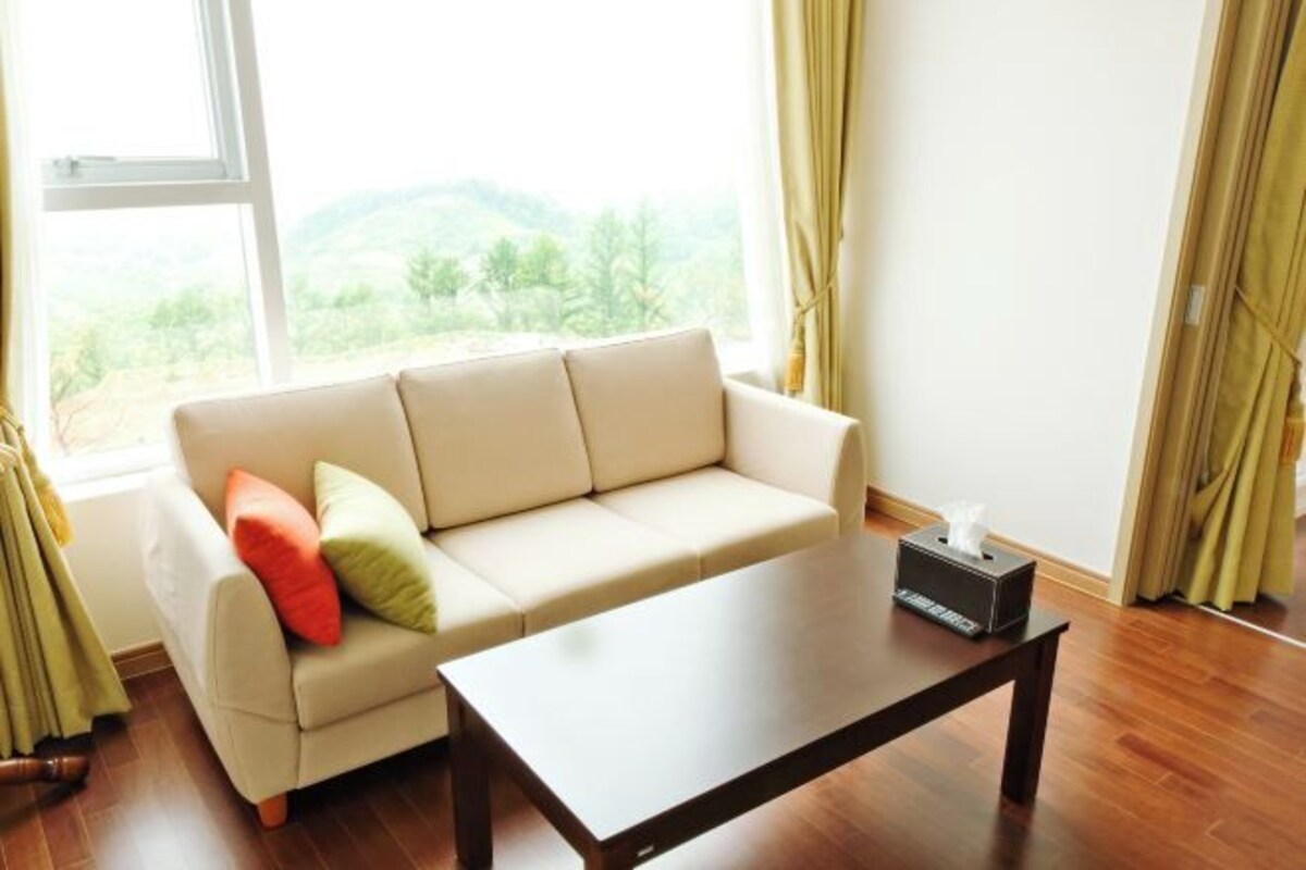 A living room with a beige sofa, a wooden coffee table, and a window with curtains.