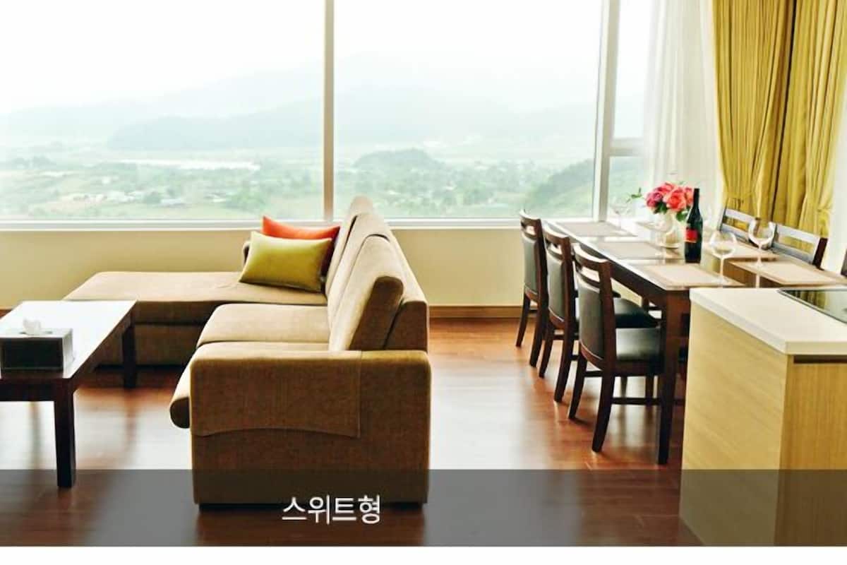 A modern living room with a sofa, a dining table, and chairs. There is a view of a cityscape through large windows.