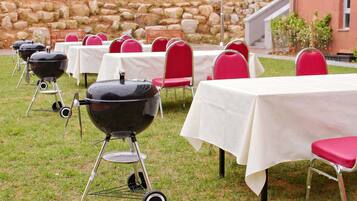 Outdoor tables with red chairs and a black grill in a grassy area.