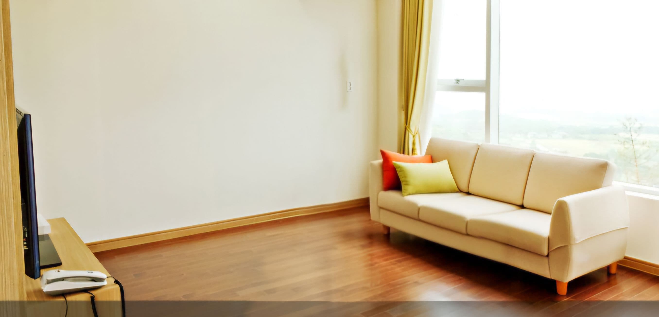 A room with a beige sofa, a flat-screen TV on a wooden table, and a window with curtains.