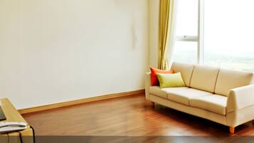 A room with a beige sofa, a flat-screen TV on a wooden table, and a window with curtains.