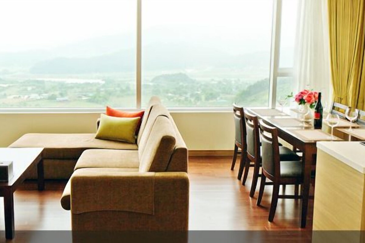 Un salon moderne avec un canapé, une table à manger et des chaises. De grandes fenêtres offrent une vue sur le paysage urbain.