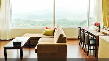 A modern living room with a sofa, a dining table, and chairs. There is a view of a cityscape through large windows.