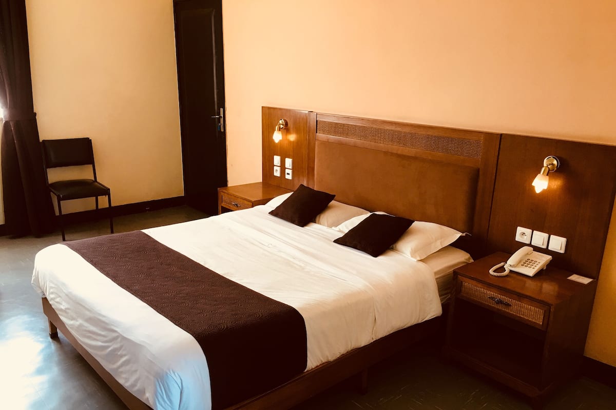 Une chambre d’hôtel avec un grand lit, deux tables de chevet, une chaise et un téléphone sur la table de nuit.