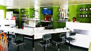 Un restaurante con paredes verdes, una barra con televisor y una variedad de botellas en estanterías.