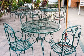 Outdoor seating with metal tables and chairs, surrounded by plants and a brick wall.