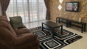 A living room with a sofa, a coffee table, a stone wall, and a TV mounted on the wall. - Little Tree Homestay at Bangi Putrajaya (Kajang)