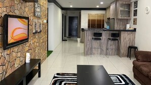 A modern living room with a stone accent wall, a flat-screen TV, a black coffee table, and a brown sofa. - Little Tree Homestay at Bangi Putrajaya (Kajang)