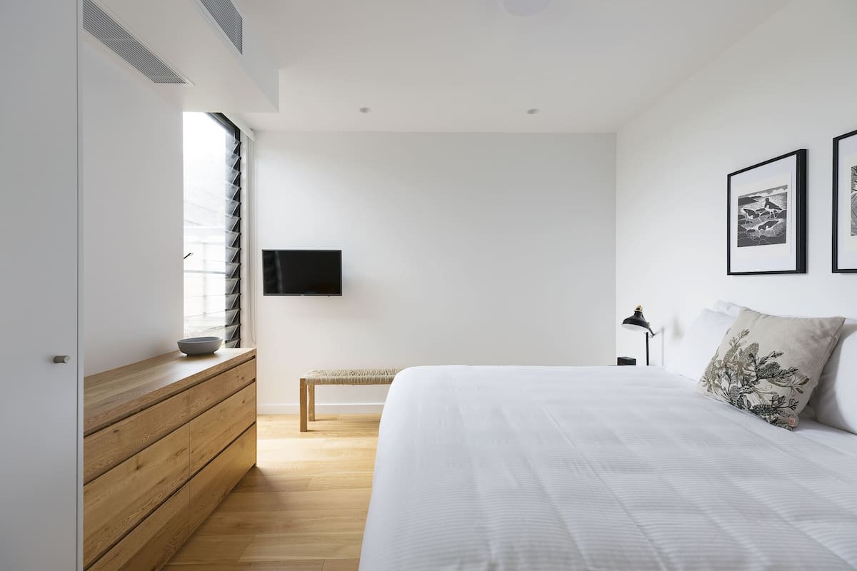Un dormitorio con cama, banco de madera, televisor y obras de arte en la pared.