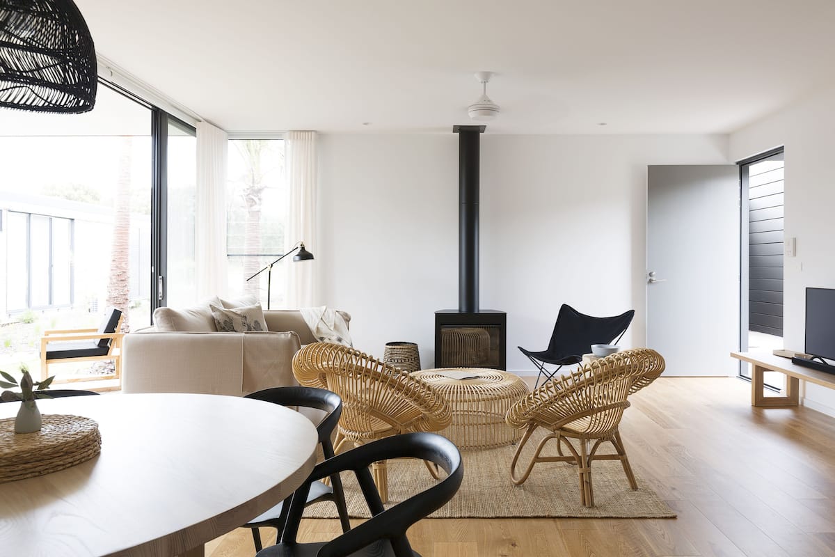 Una sala de estar moderna con un sofá, dos sillones de mimbre, una mesa redonda, un televisor y una chimenea.